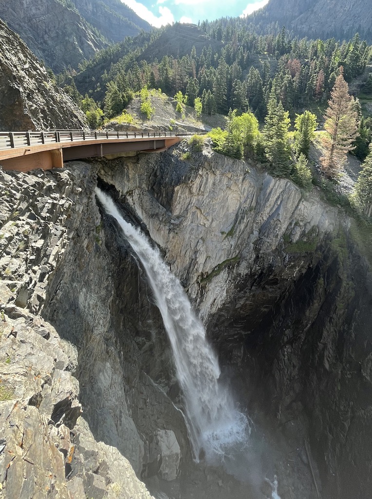 Waterfall coming out of chasm below highway with mountain peak views in background. Bear Creek Falls Scenic Overlook, Million Dollar Highway, near Ouray, Colorado.