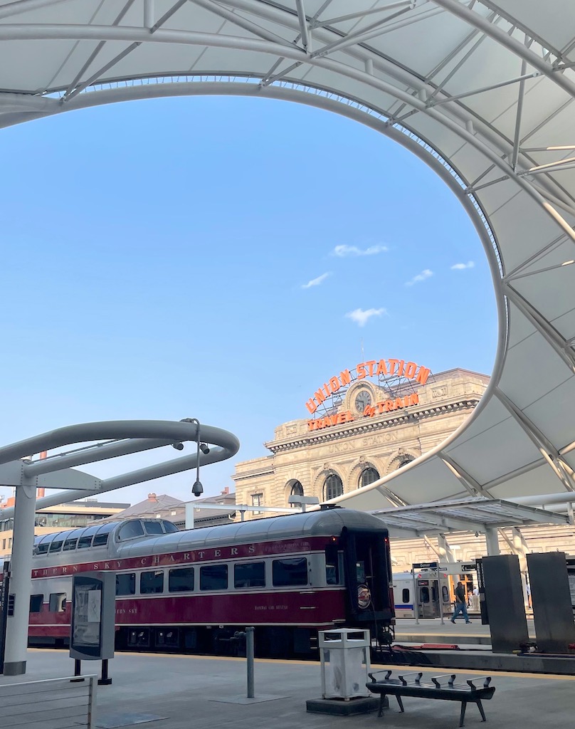 Old, red train car surrounded by modern train station on sunny day. Denver Union Station, Denver, Colorado. Things to do in Denver with one day, things to do in Denver during a layover.