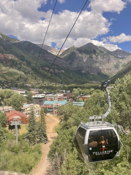 View from Telluride gondola over town of Telluride and other gondola pods with dramatic mountain views in background on sunny summer day. Telluride Gondola, Telluride, Colorado.