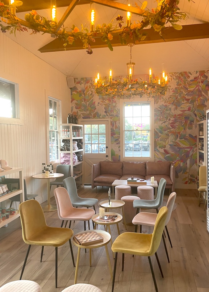 Interior with pastel chairs and tables, floral wall, hardwood floors, and large light fixtures. Interior of Kidd Squid Brewing Company, Sag Harbor, New York, The Hamptons.