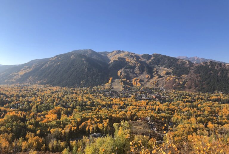 Sweeping views of downtown Aspen covered in yellow fall colors with mountain peaks in background on cloudless autumn day. Hunter Creek Valley, Aspen, Colorado.