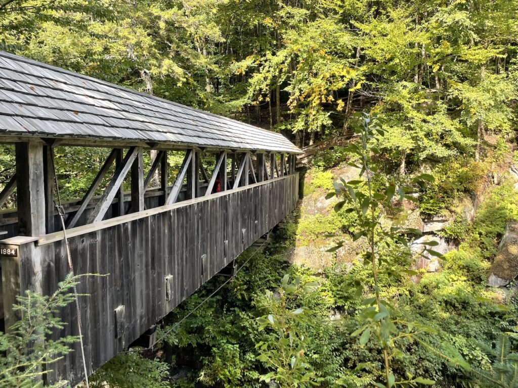 Wooden covered bridge over river surrounded by lush greenery in mountains. Sentinel Pine Covered Bridge, Flume Gorge, Franconia Notch State Park, White Mountains, New Hampshire.