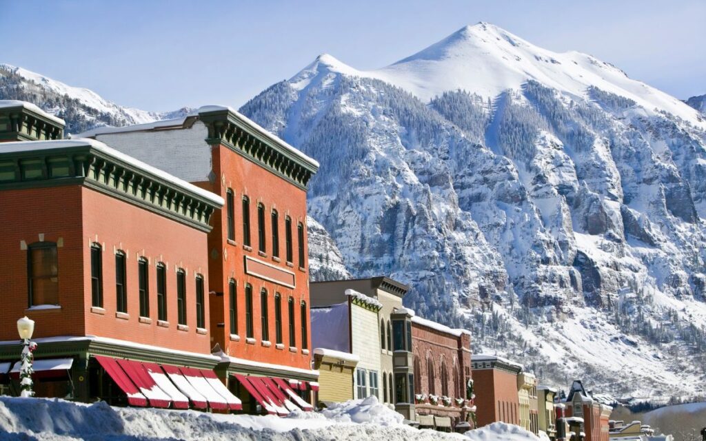 Small town with mining-era buildings lining simple main street with huge mountain peak covered in snow in background. Telluride, Colorado in winter.