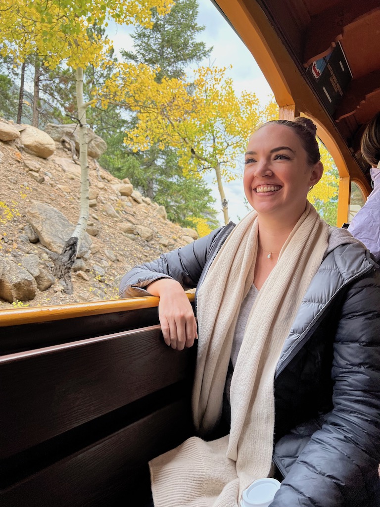 Woman smiling on open air train with yellow fall colors and mountain views in background. Georgetown Loop Railroad train ride in fall, Georgetown, Colorado.