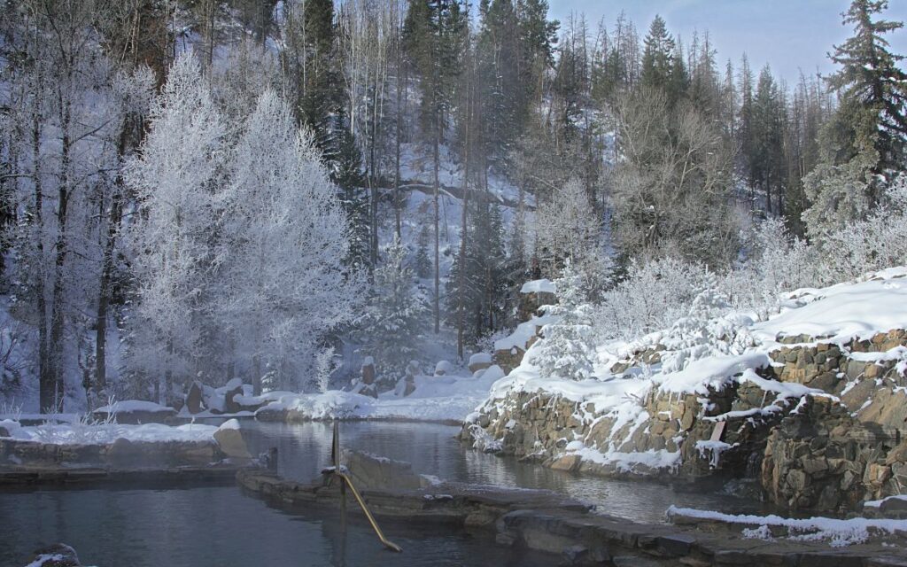 Hot springs in a mountain setting surrounded by snow covered forest and rocky area on early morning in winter. Strawberry Hot Springs in winter, Steamboat Springs, Colorado.
