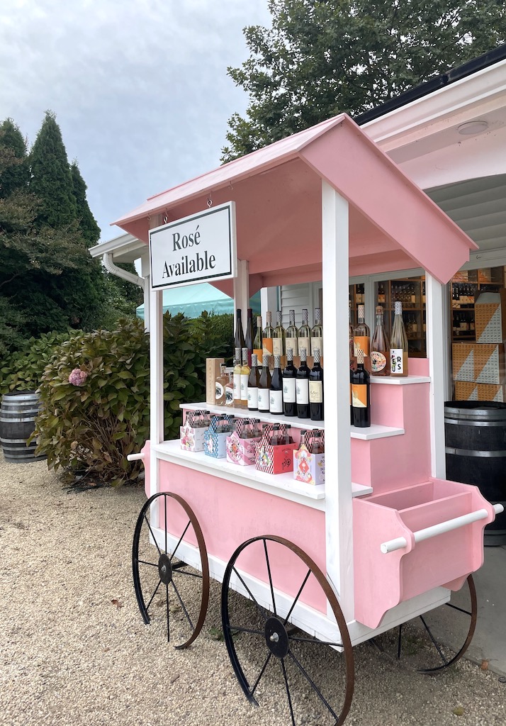 Pink wine car with wine bottles on display and sign reading "Rosé Available" on gloomy, early fall day. Wölffer Estate Wine Stand, Sagaponack, New York, The Hamptons