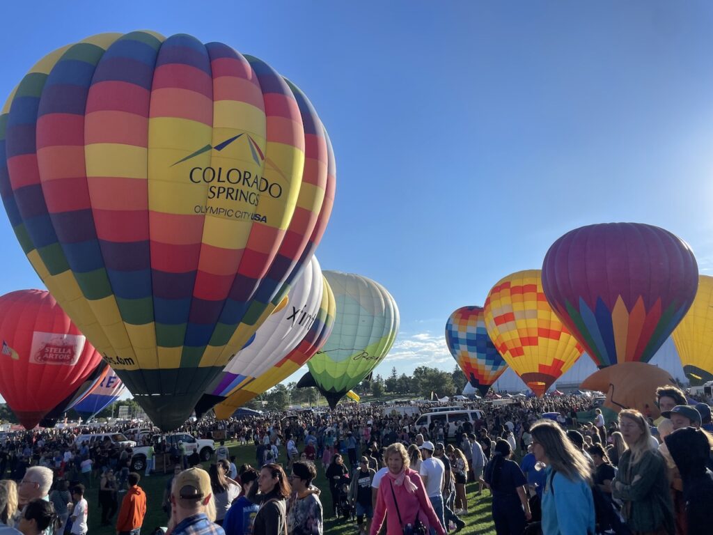 Colorful hot air balloons filled with air but still on the ground, surrounded by huge crowds of people at hot air balloon festival on sunny summer morning. Colorado Springs Labor Day Lift Off, Colorado Springs, Colorado.