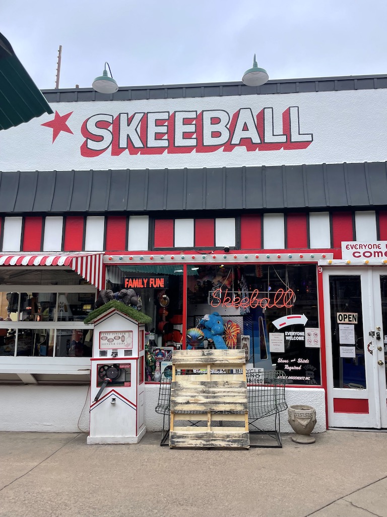 Storefront of arcade with large sign reading "Skeeball" with colorful striped awning and decor on winter day. Manitou Springs Penny Arcade, Manitou Springs, Colorado Springs, Colorado.