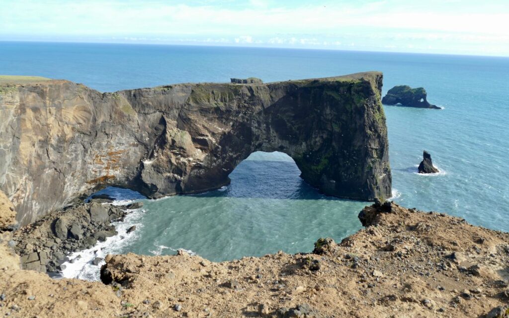 Rocky arch formation in bright blue waters of Northern Atlantic Ocean. Arch Rock, Dyrhólaey Viewpoint, South Coast, Iceland.