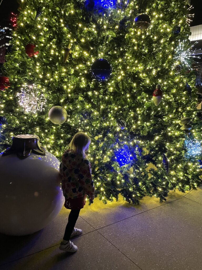 Silhouette child next to giant ornament and giant Christmas tree, lit up at night. RiverFront Park Gene Leahy Mall, tree lighting, Omaha, Nebraska.