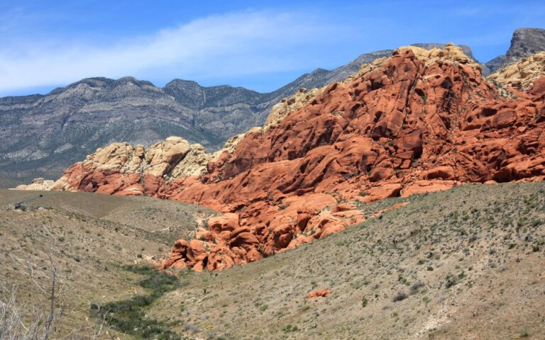 Huge, bright red rocks surrounded by brown and green desert landscape on sunny day. Red Rock Canyon National Conservation Area, day trip from Las Vegas, Nevada.