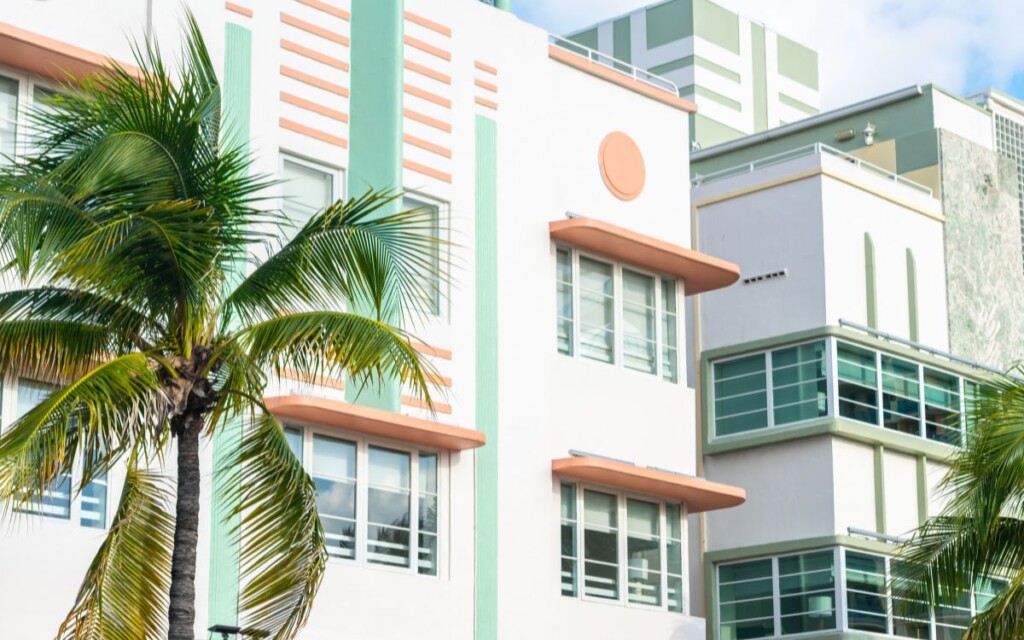 White building with pastel teal and orange designs, palm tree in the foreground. Art Deco Buildings, Ocean Drive, Art Deco District, South Beach, Miami, Florida.