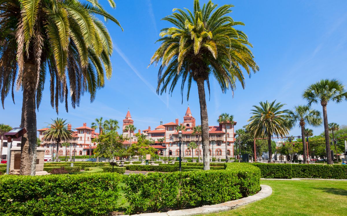 Historic building with ornate orange trim and Spanish-style architecture framed by palm trees and neat, green gardens. Flagler College, St. Augustine, Florida.