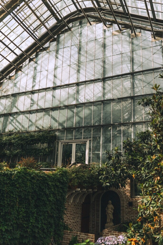 Large greenhouse with tall glass windows and glass ceiling, greenhouse is full of greenery and flowers. Lauritzen Gardens, Omaha, Nebraska.