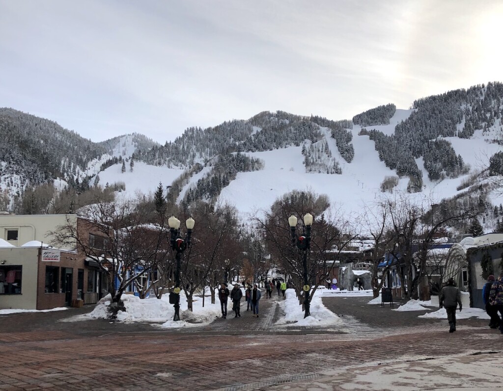 Snow-covered ski mountain overlooking brick sidewalks and pedestrian mall on cloudy winter day. Mill Street Mall, Downtown Aspen, Colorado.