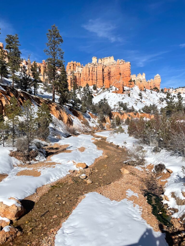 Small stream winding through red rock landscape covered in snow on sunny winter day. Mossy Cave hike, Bryce Canyon National Park, Utah.