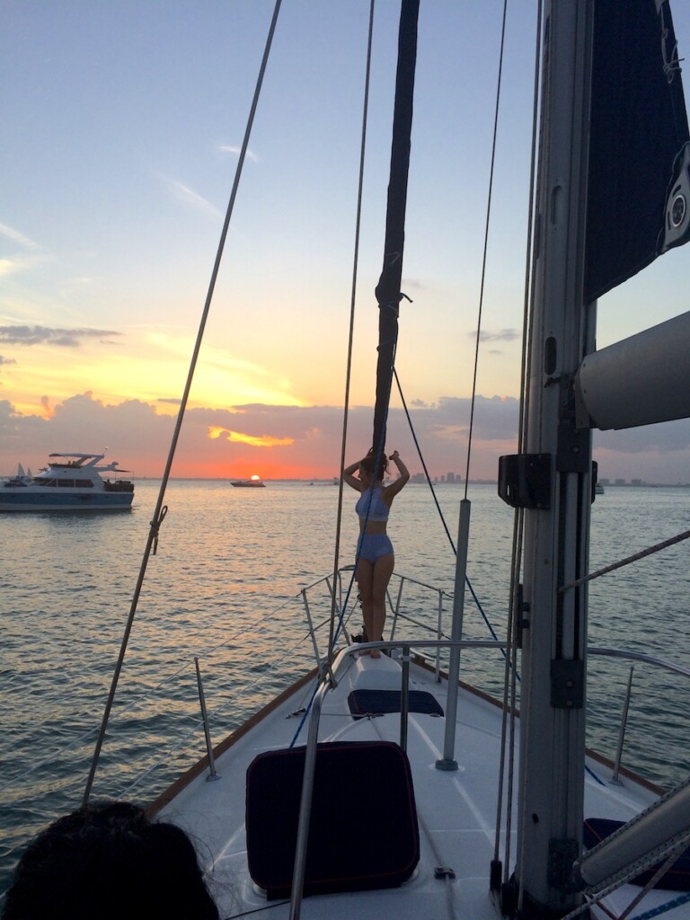 Silhouette of woman at helm of sailboat with yacht in near distance during colorful sunset. Sunset sail, Biscayne Bay, South Beach, Miami, Florida.