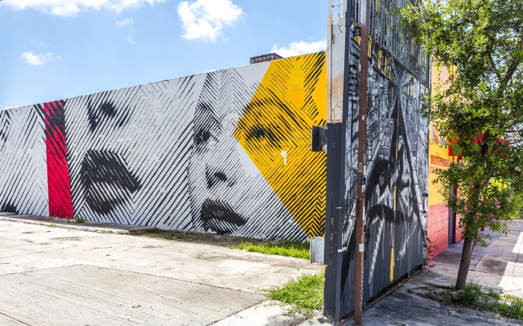 Walls covered in elaborate graffiti street art, paintings of people's faces and city-scapes on sunny afternoon. Wynwood Walls, Miami, Florida.