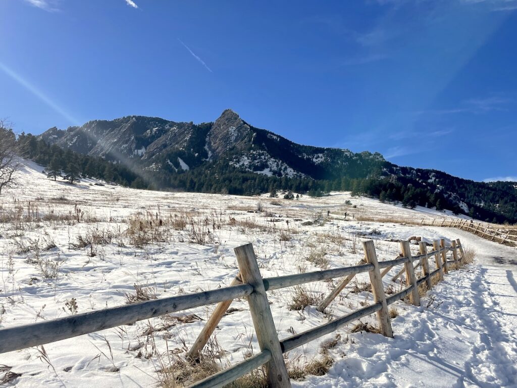 Snow-covered field with jagged mountains in background on sunny winter day. Chautauqua Park, Boulder Flatirons, Boulder, Colorado.