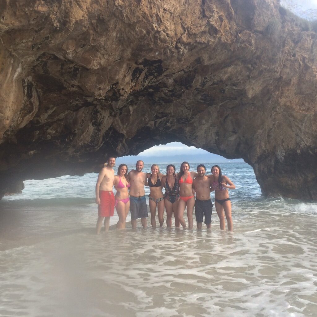 Group of friends under large rocky arch on shore of Pacific Ocean. Marietas Islands National Park, Riviera Nayarit region, Mexico.