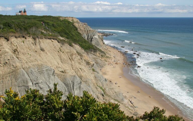 Beach bluffs overlooking blue Atlantic Ocean with lighthouse in distance on sunny summer day. Mohegan Bluffs beach, Block Island, Rhode Island, New England.
