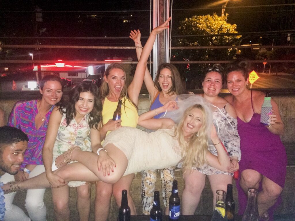 Group of women celebrating bachelorette party, smiling and laughing at camera on rooftop patio of bar. Bachelorette Party, Austin, Texas.