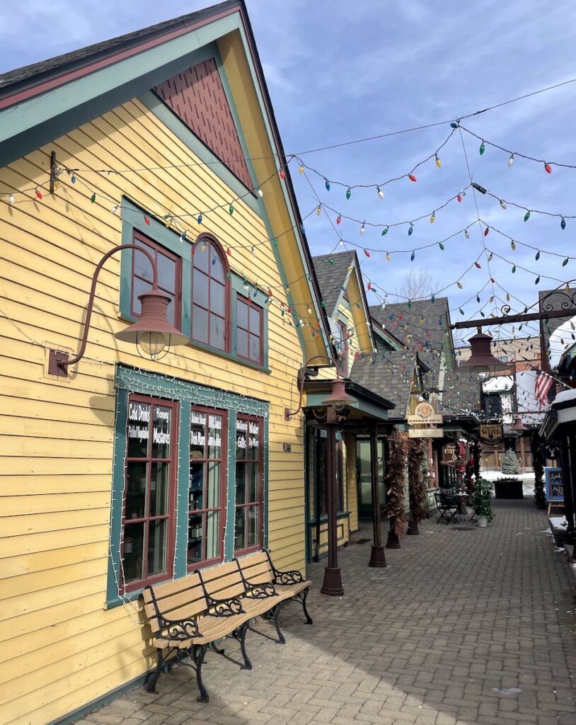 Colorful shingled homes next to brick sidewalks, benches, and colorful string lights on sunny winter day. Breckenridge Historic District, Main Street, Breckenridge, Colorado.