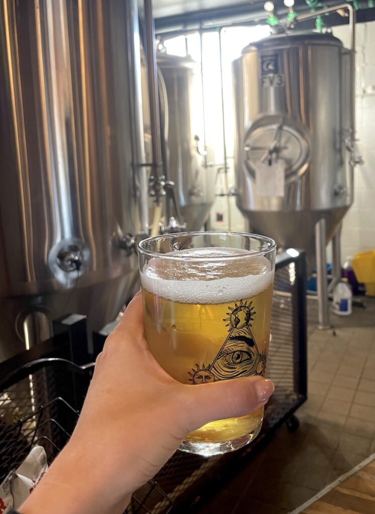 Woman holding craft beer in front of steel drums in brewery. Avant Garde Aleworks, Estes Park, Colorado.
