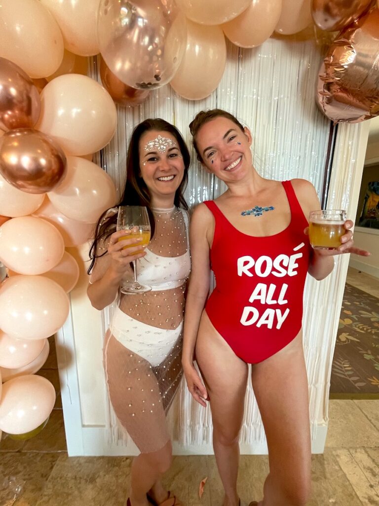 Bride-to-be and friend posing in front of balloon wall with wine during bachelorette party weekend pool day. Napa Valley, California.