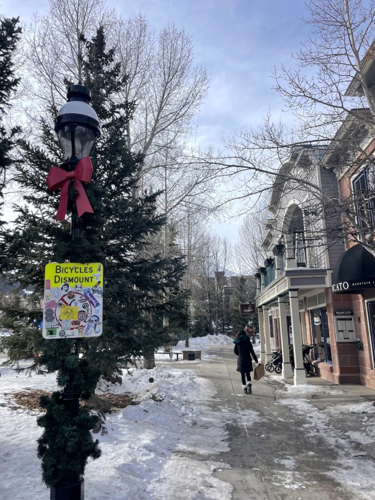 Snowy sidewalk lined with shops and pine trees on sunny winter day. Breckenridge Historic District, Main Street, Breckenridge, Colorado.