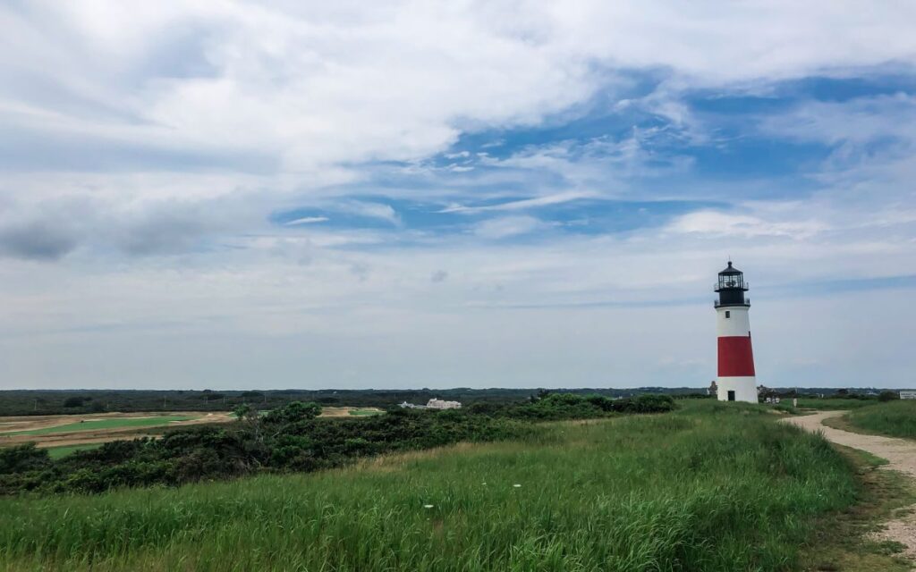 White and red striped lighthouse in green field on sunny summer day. Sankaty Head Light, Nantucket, Cape Cod, Massachusetts.