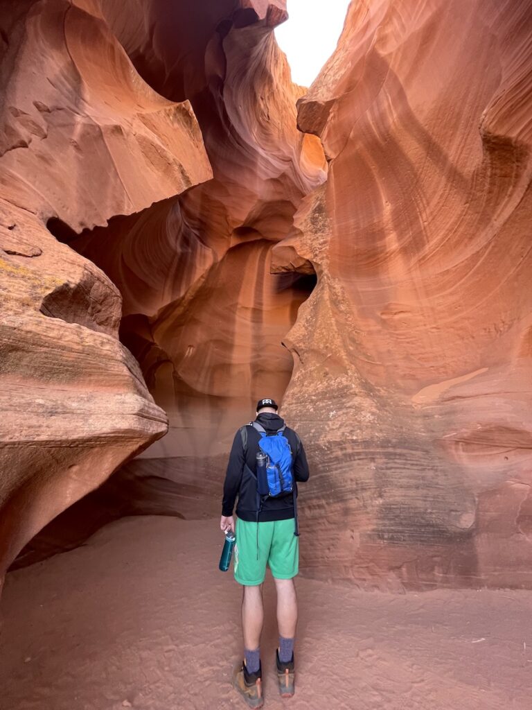 Man standing at entrance of bright orange slot canyon. Upper Antelope Canyon, Page, Arizona.