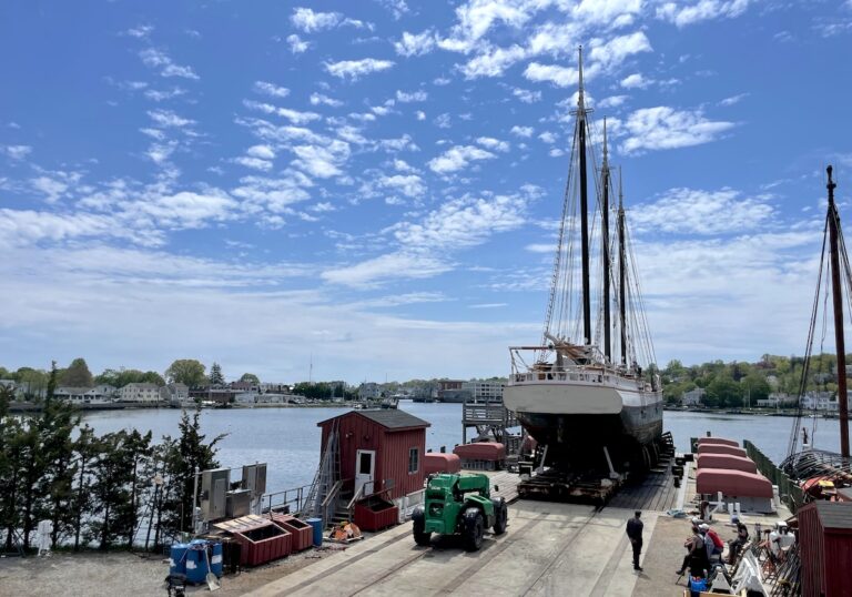 Three-masted wooden schooner ship on repair dock over river on sunny day. Maritime Seaport Museum, Mystic, Connecticut.