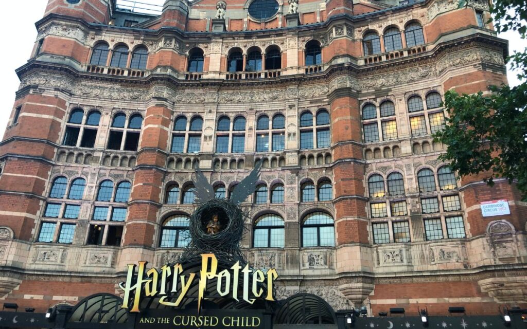 Red brick building with architectural details and large sign reading "Harry Potter and the Cursed Child" on sunny day. Palace Theatre, London, England, United Kingdom.