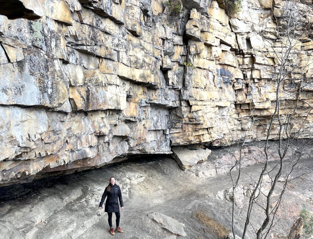 Woman standing under rocky cliff on hiking trail in fall. Castle Rock Trail, New River Gorge National Park, West Virginia.