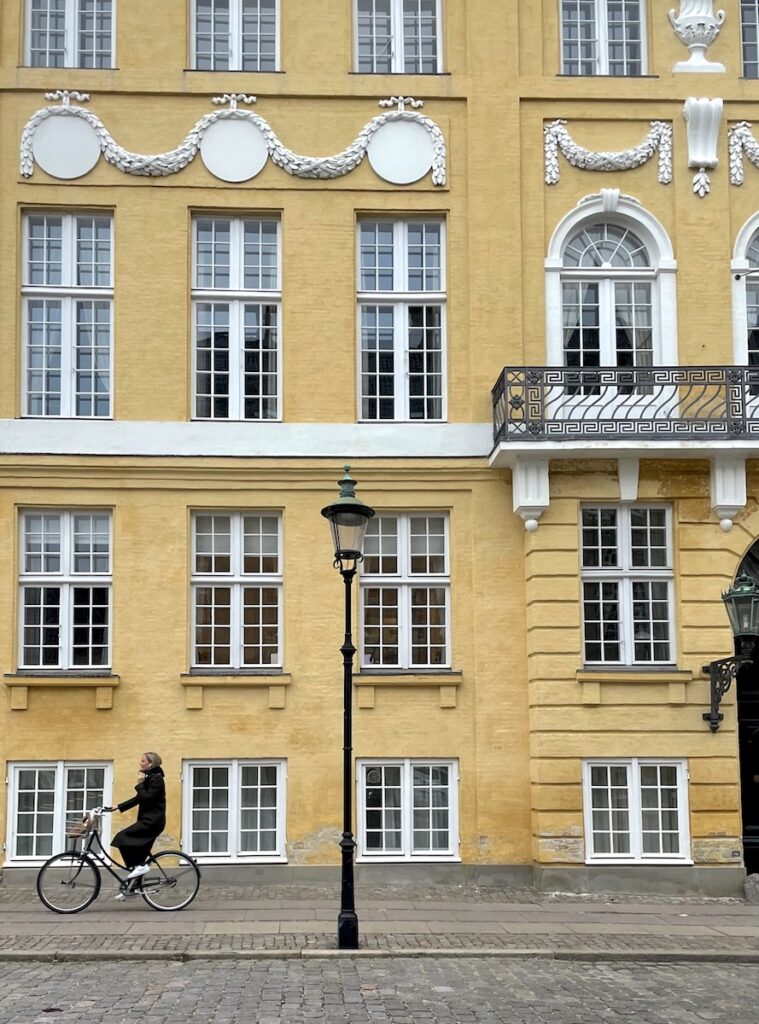 woman biking yellow building copenhagen denmark
