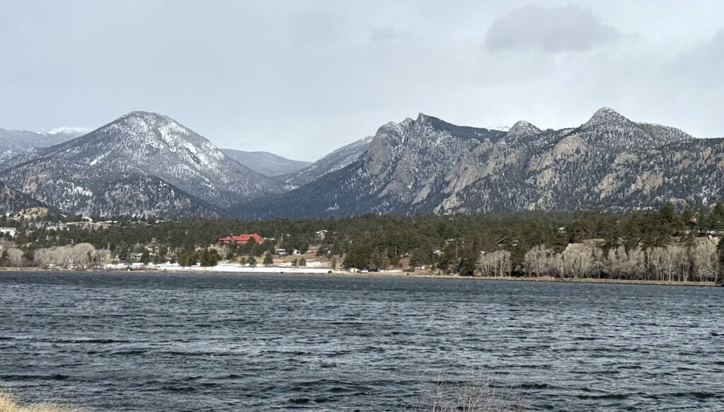 Snow-capped mountain peaks overlooking choppy lake on windy, grey spring day. Lake Estes, Estes Park, Colorado.