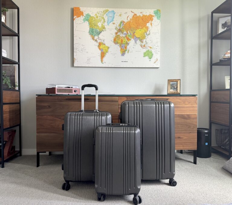 Three grey hardshell suitcases in front of dresser and large world map in bedroom. Coolife hardshell luggage 3-pack in grey.