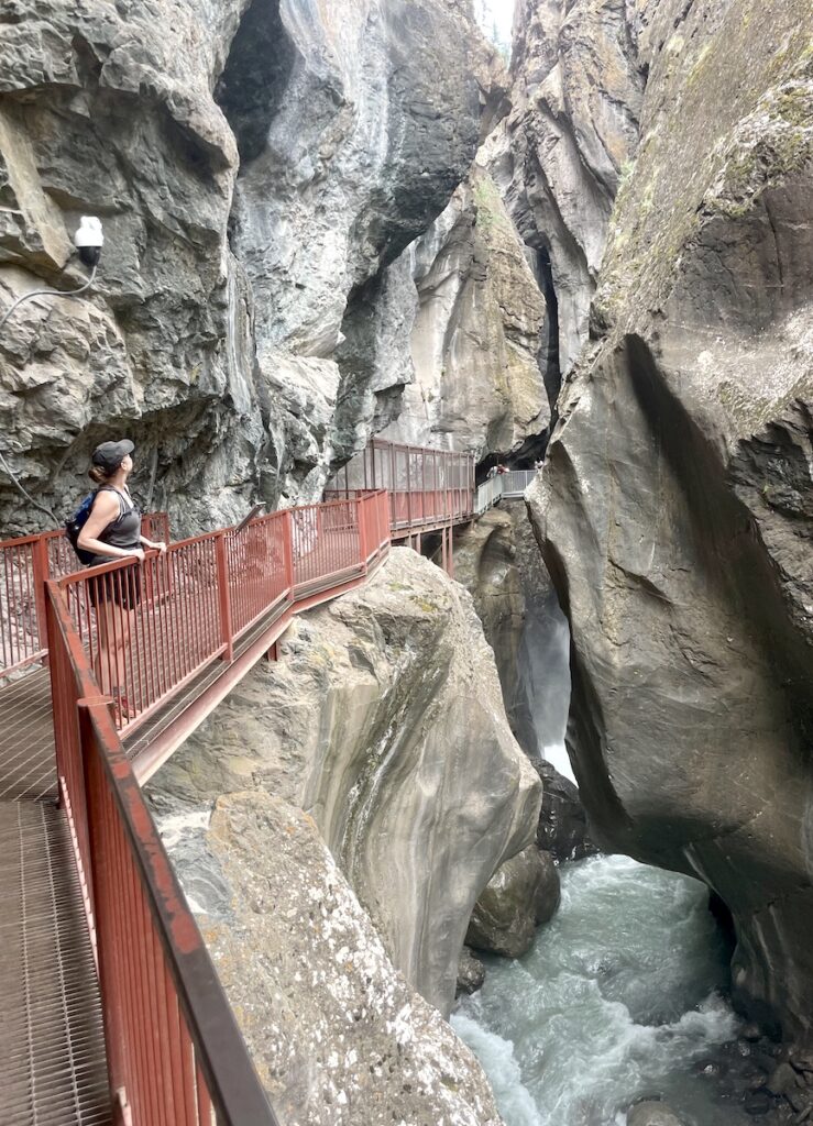 Woman on walkway in narrow box canyon with waterfall rushing through narrow chasm in summer. Box Canyon Falls, Ouray, Colorado.