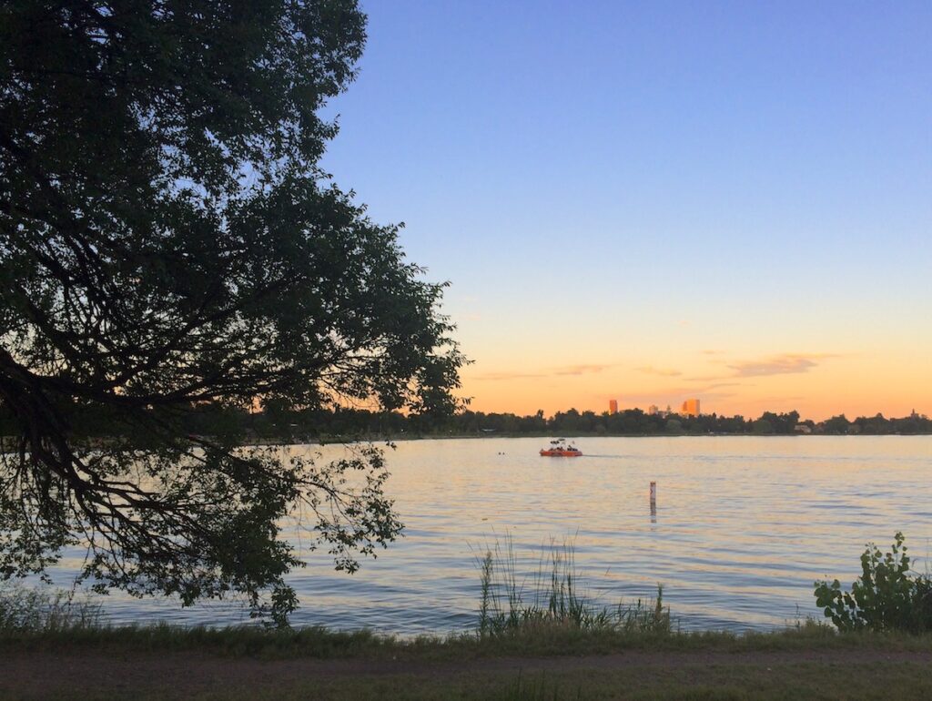 Sunset over lake during sunset with small boat on lake and city skyline in distance. Sloan's Lake, Denver, Colorado.