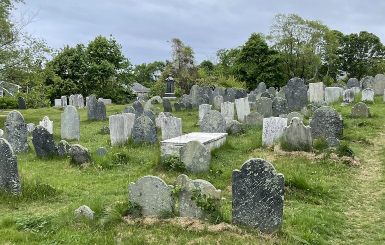 Old graveyard with small, simple tombstones in grassy hill on gray, cloudy day. Old Burial Hill Cemetery, Marblehead, Massachusetts, near Salem.