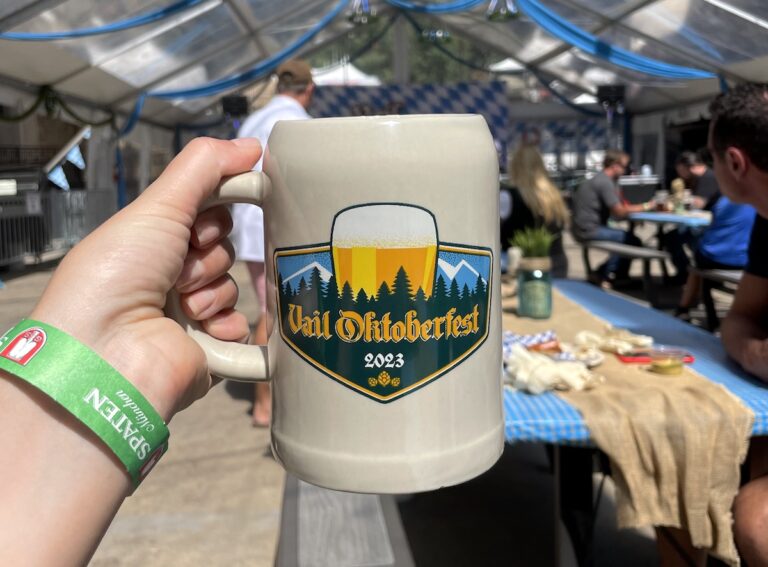 Ceramic beer stein with Vail Oktoberfest logo, with German beer tent and live band in background. Vail Oktoberfest, Vail, Colorado.