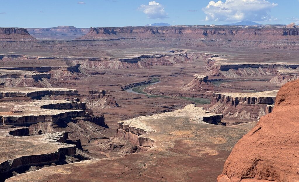 Sweeping canyon views of red canyon with river flowing through it on sunny day. Green River Overlook, Canyonlands National Park, Island In The Sky, Moab, Utah.
