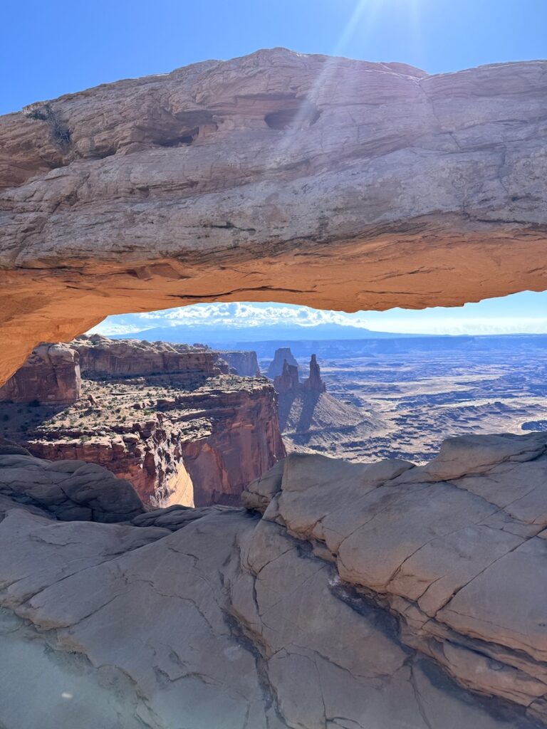 Low, long natural sand stone arch in desert with canyon views in distance on sunny morning. Mesa Arch Hike, Canyonlands National Park, Island In The Sky, Moab, Utah.