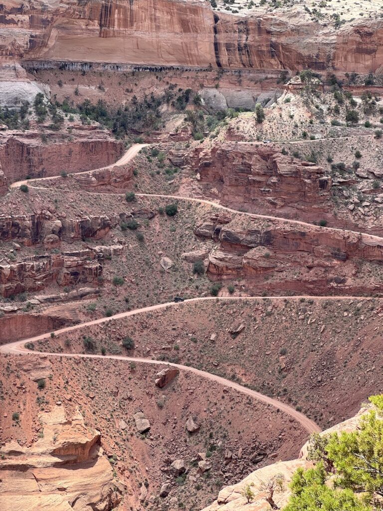 Dirt road switchbacks winding through huge red rock canyon in summer. Shafer Canyon Road from Shafer Canyon Overlook, Canyonlands National Park Island In The Sky, Moab, Utah.