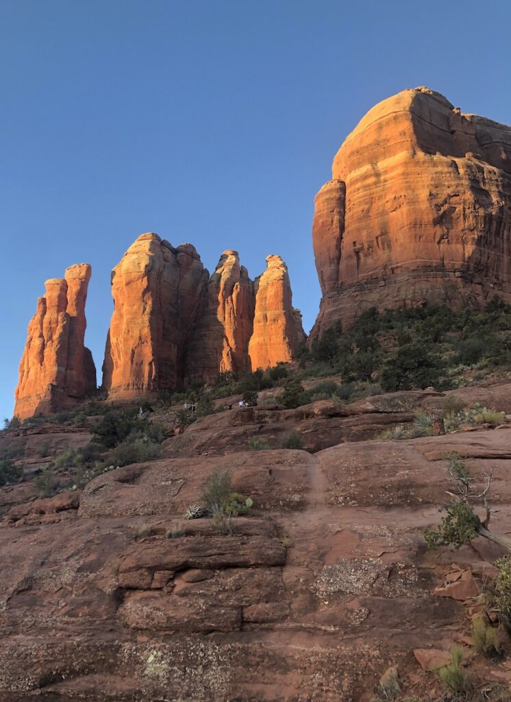 Red rock mountain spires lit bright red during sunrise with bright blue sky in background. Hiking Cathedral Rock Trail, Sedona, Arizona.