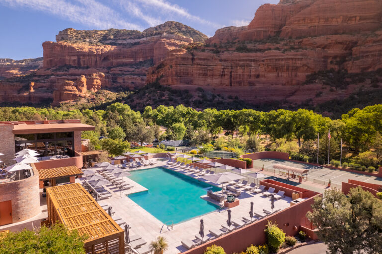 Luxury hotel pool surrounded by lounge chairs and dramatic red rock cliffs on sunny summer day. Enchantment Resort, Sedona, Arizona. Drone Photo Credit: Kevin Floerke