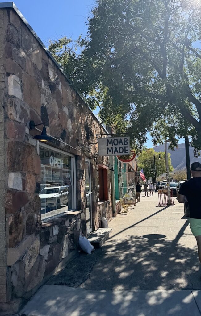 Stone-facade building under shade of large tree on sunny afternoon. Shopping district, downtown Moab, Utah.