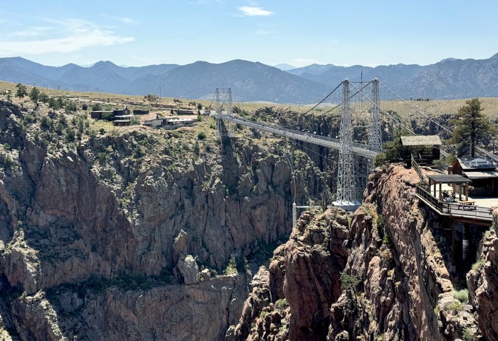 Large suspension bridge spanning huge, rocky gorge with mountain views in background on sunny day. Royal Gorge Bridge, Royal Gorge, Cañon City, Colorado.