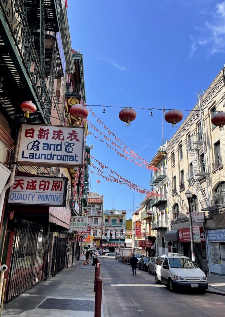 Shopping and dining district with large signs in English and Chinese characters and string decorations over the street on sunny day. Chinatown, San Francisco, California.